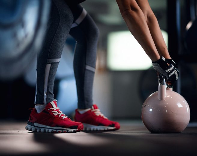 Unrecognizable sportswoman practicing with kettle bell on cross training in fitness center.